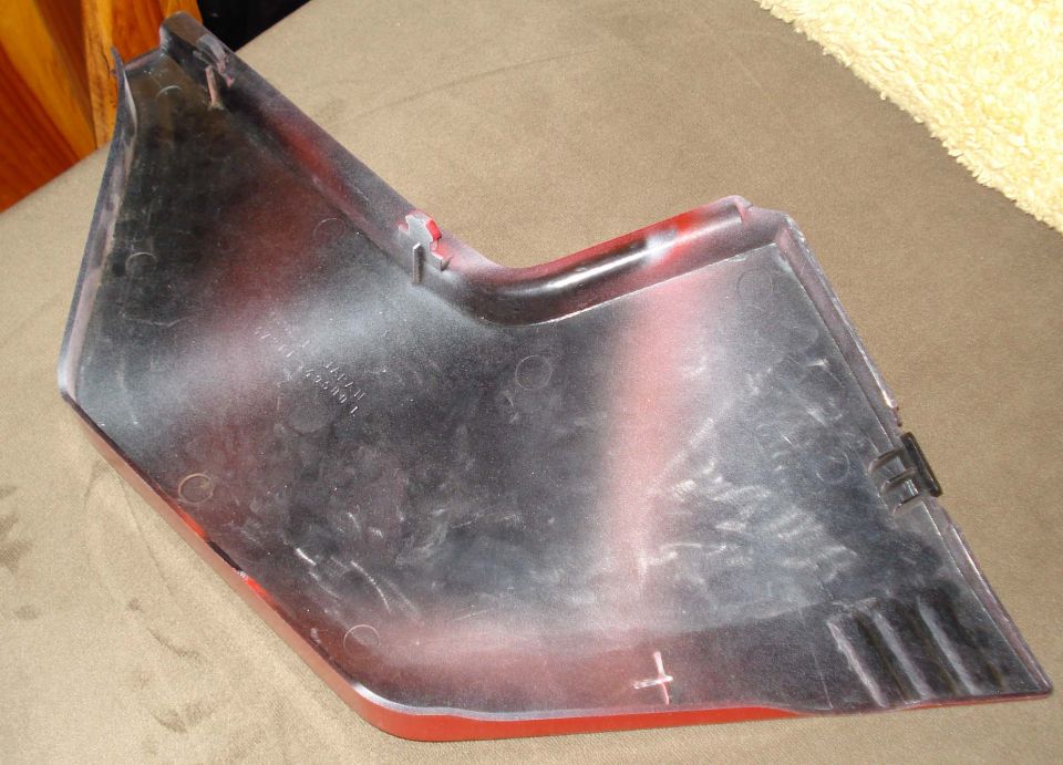 Close-up of a red and silver car fender trim piece with some markings and clips