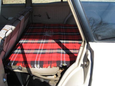 1966 Ford Falcon - The rear seat of a car is covered with a red and black plaid blanket.