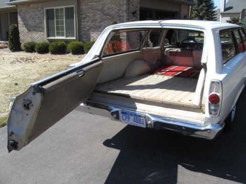 1966 Ford Falcon - The rear of a white 1966 Ford Falcon station wagon is shown with its tailgate open, revealing the cargo area.