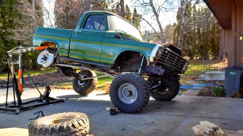 1967 Ford F-250 - A green pickup truck is undergoing maintenance, with its front end elevated by a hydraulic lift and one wheel removed.