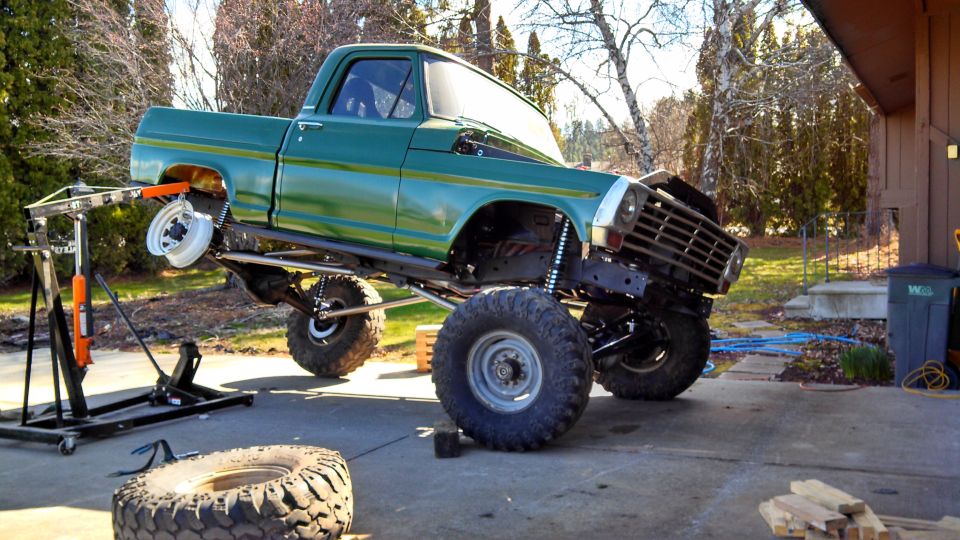 Green pickup truck with lifted suspension and large tires, front wheel removed and supported by a lift