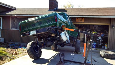 1967 Ford F-250 - Green Ford pickup truck with custom suspension is being worked on in a driveway.