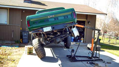1967 Ford F-250 - A green 1967 Ford F-250 pickup truck is shown from the rear, a lifted suspension and an engine hoist nearby.