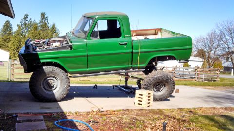 1967 Ford F-250 - A green 1967 Ford F-250 pickup truck is parked outside with its hood up, showing off its engine and lifted suspension.