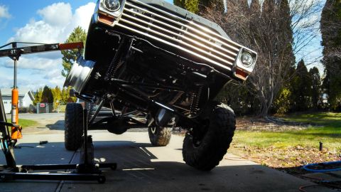 1967 Ford F-250 - A heavily modified Ford F-Series truck is suspended by an engine hoist, revealing its lifted suspension and undercarriage.