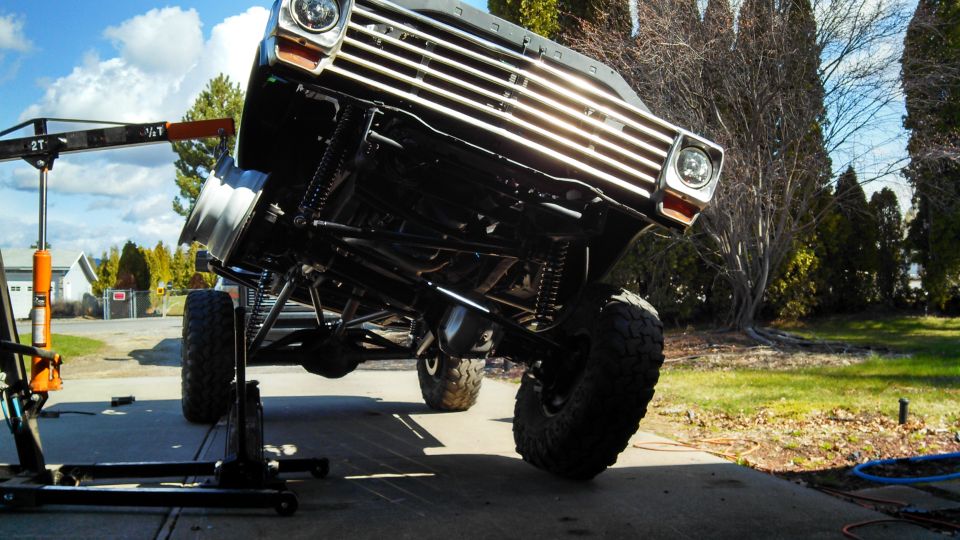 Front view of a lifted Ford F-Series truck with a chrome grille, being worked on with an engine hoist