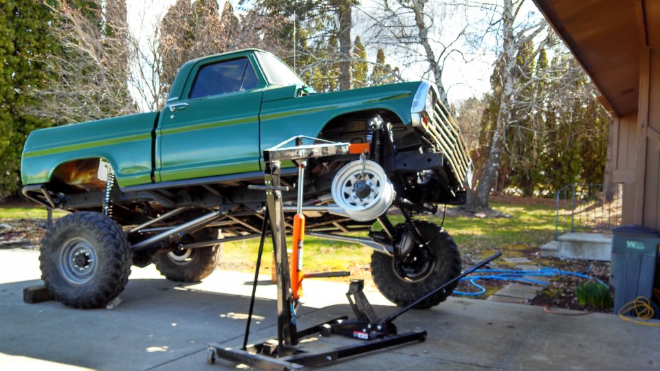 Green pickup truck with lifted suspension, front end disassembled, parked in driveway