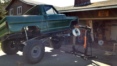 1967 Ford F-250 - A green pickup truck is undergoing modifications in front of a garage, with its front end supported by a lift.