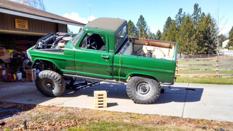 1967 Ford F-250 - A green 1967 Ford F-250 pickup truck is parked in a driveway with its hood open and suspension lifted.