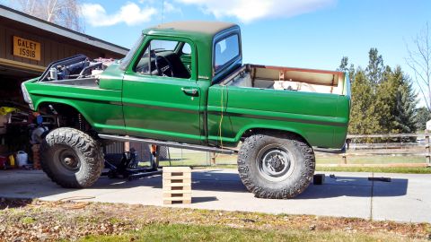 1967 Ford F-250 - This green 1967 Ford F-250 pickup truck is undergoing modifications with its hood open and suspension lifted.