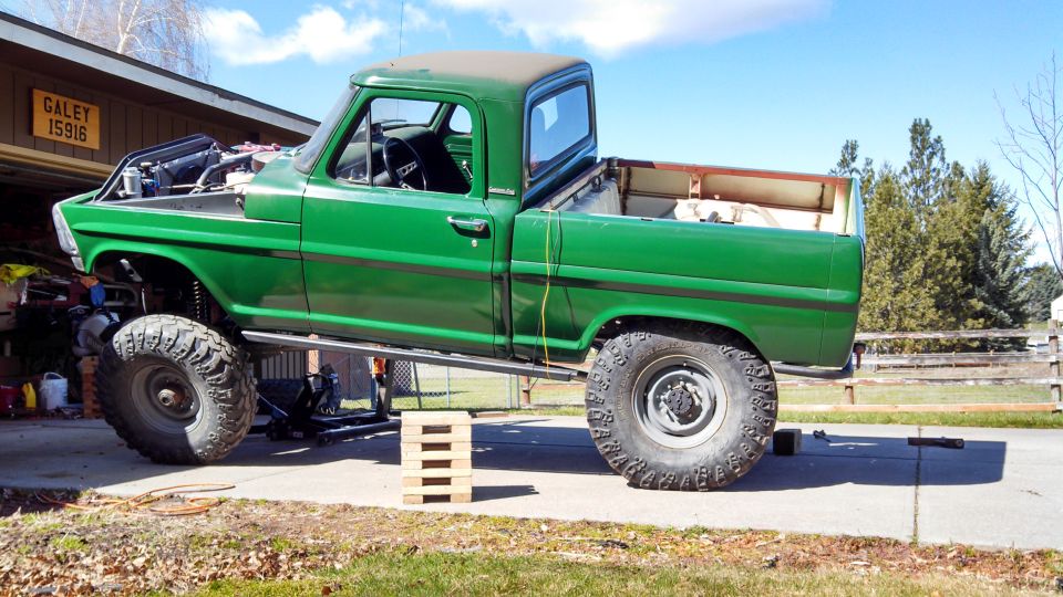 Green 1967 Ford F-250 pickup truck with lifted suspension and large tires, parked outside a garage