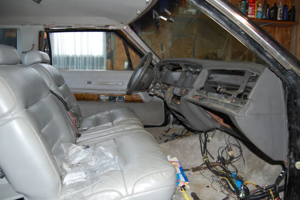 Car interior with gray leather seats, exposed dashboard wiring, and wood trim. The dashboard is partially disassembled