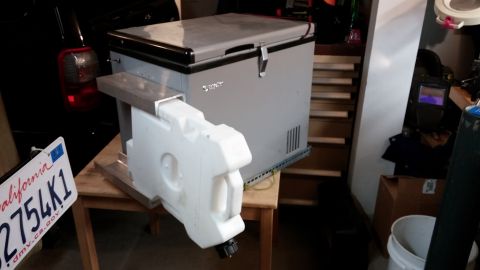 1985 Toyota 4Runner - A custom mount holds a portable refrigerator and a water jug, with a vehicle's rear visible.