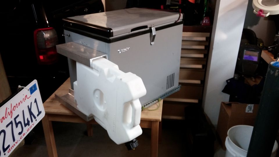 Portable fridge and water jug mounted on a metal bracket, with a California license plate nearby