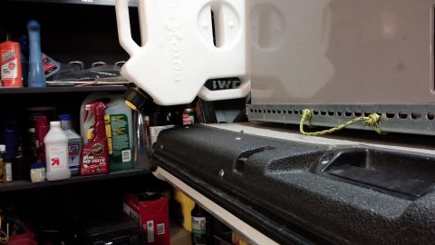 1985 Toyota 4Runner - A Rotopax fuel container is mounted to the exterior of a vehicle, with various automotive fluids visible on shelves behind it.