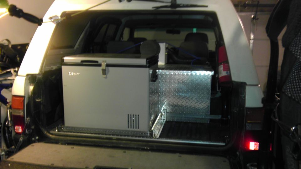 White 1985 Toyota 4Runner rear cargo area with a silver refrigerator and diamond plate toolbox on a slide-out tray