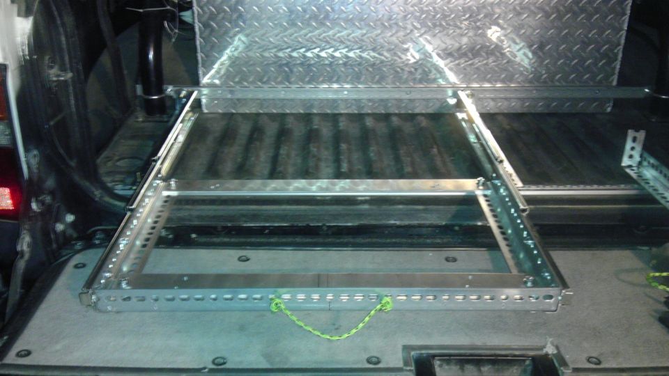 Inside of a vehicle with a metal cargo slide-out tray installed. Diamond plate metal is visible above the tray