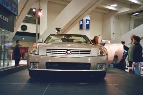 1992 Mercury Grand Marquis - Silver Cadillac XLR convertible displayed at an auto show, with people observing the vehicle.