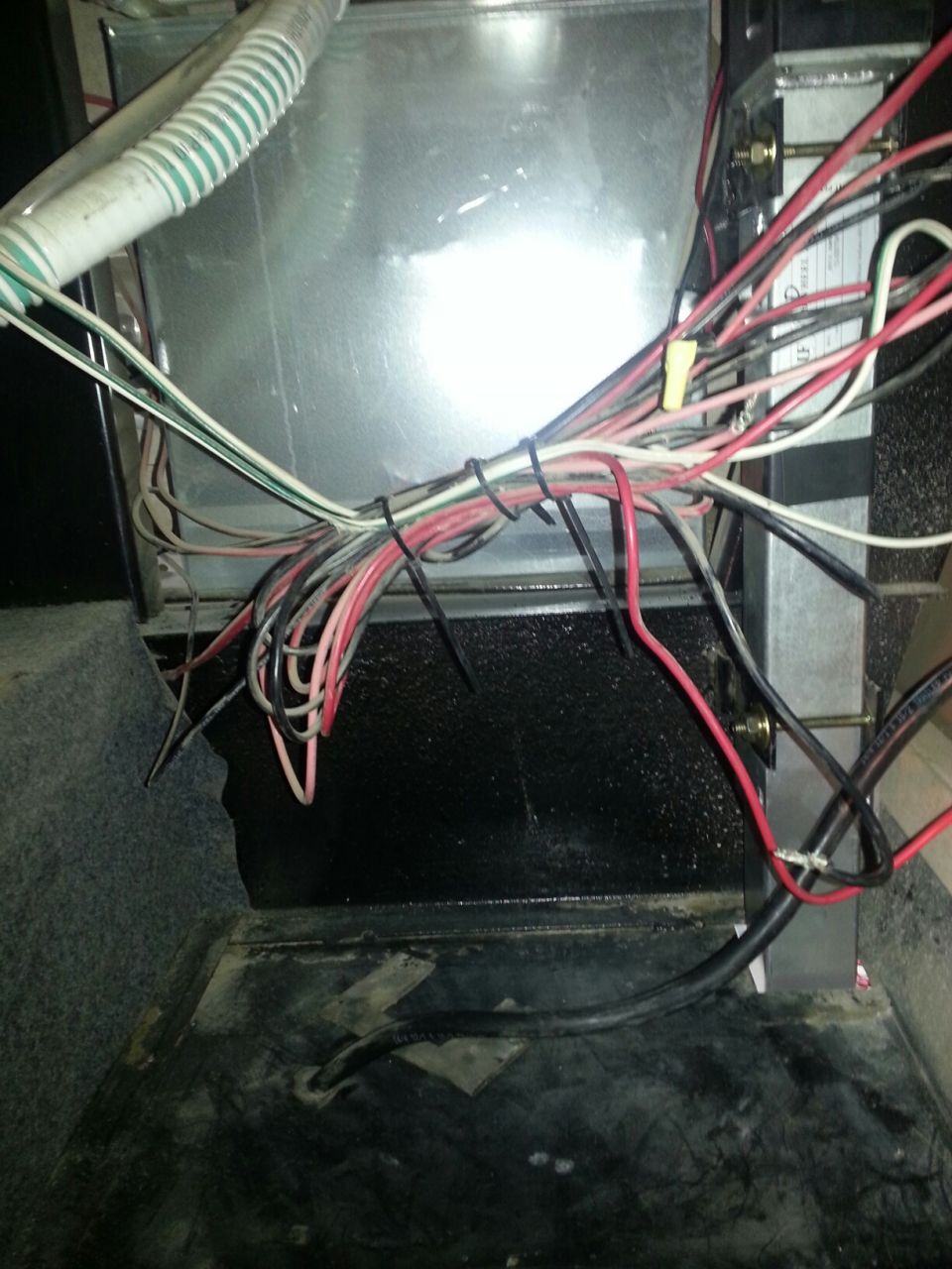 Close-up of a tangled wiring harness connected to a metal casing with a ribbed hose. Some wires are red, black, and white