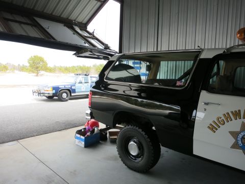 1991 Ford LTD Crown Victoria - A black and white highway patrol SUV is parked inside a hangar next to a blue state police car.