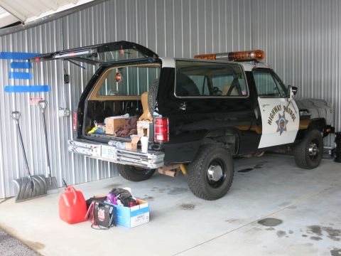 1991 Ford LTD Crown Victoria - A black and white Dodge Ramcharger SUV, marked as Highway Patrol, is parked inside a garage with its tailgate open, revealing stored items.