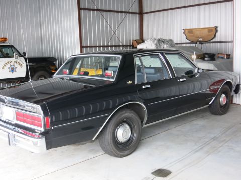 1991 Ford LTD Crown Victoria - A black sedan is parked inside a garage next to a highway patrol vehicle.