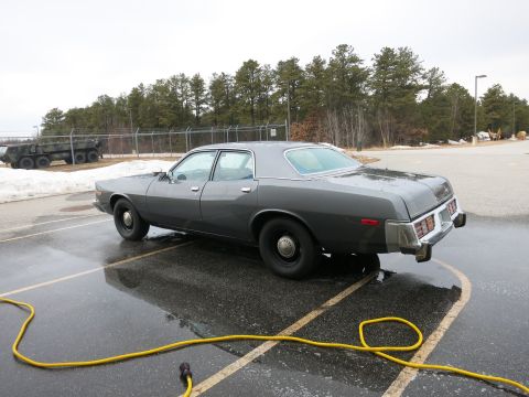 1991 Ford LTD Crown Victoria - A dark gray sedan is parked on a wet asphalt surface with a yellow hose coiled nearby.