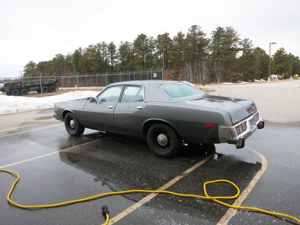 Gray sedan parked on wet asphalt, yellow hose on ground