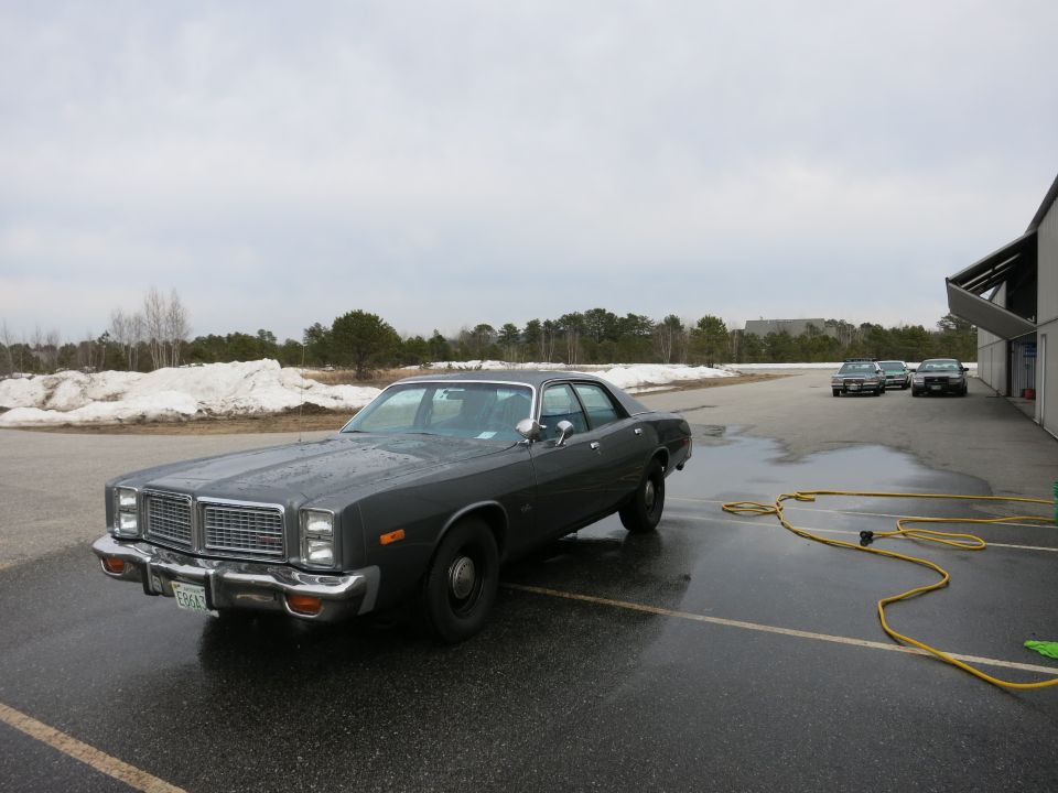 Dark gray sedan with a chrome grille and rectangular headlights parked on wet asphalt