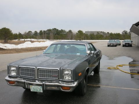 1991 Ford LTD Crown Victoria - A gray 1977 sedan is parked outside on a wet asphalt lot with other vehicles in the background.