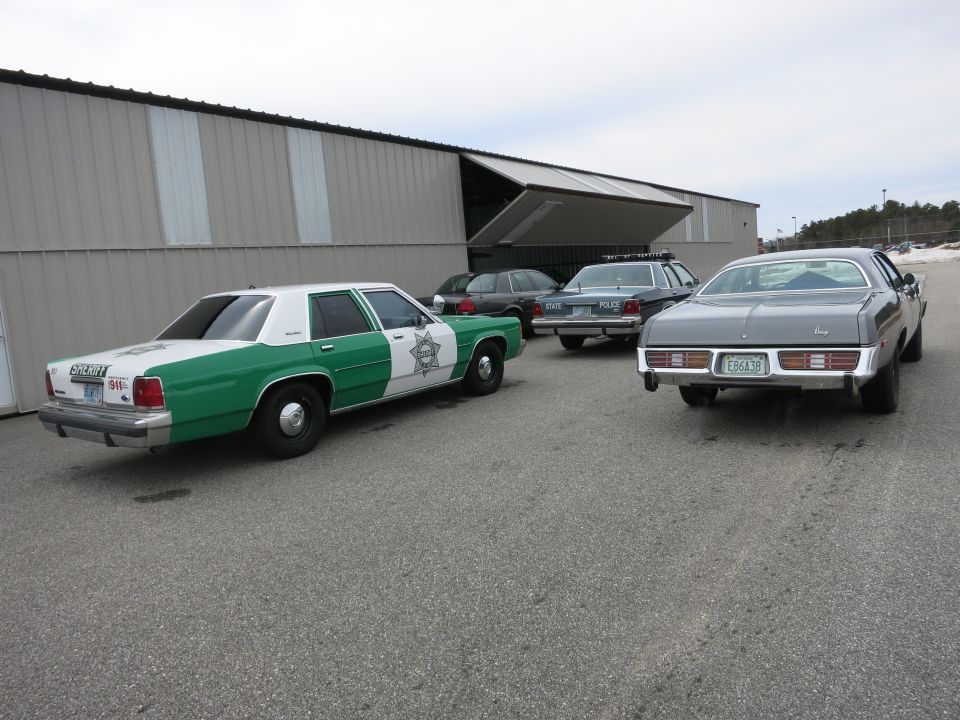 gray sedan parked near a green and white sheriff's car and two police cars by a large building