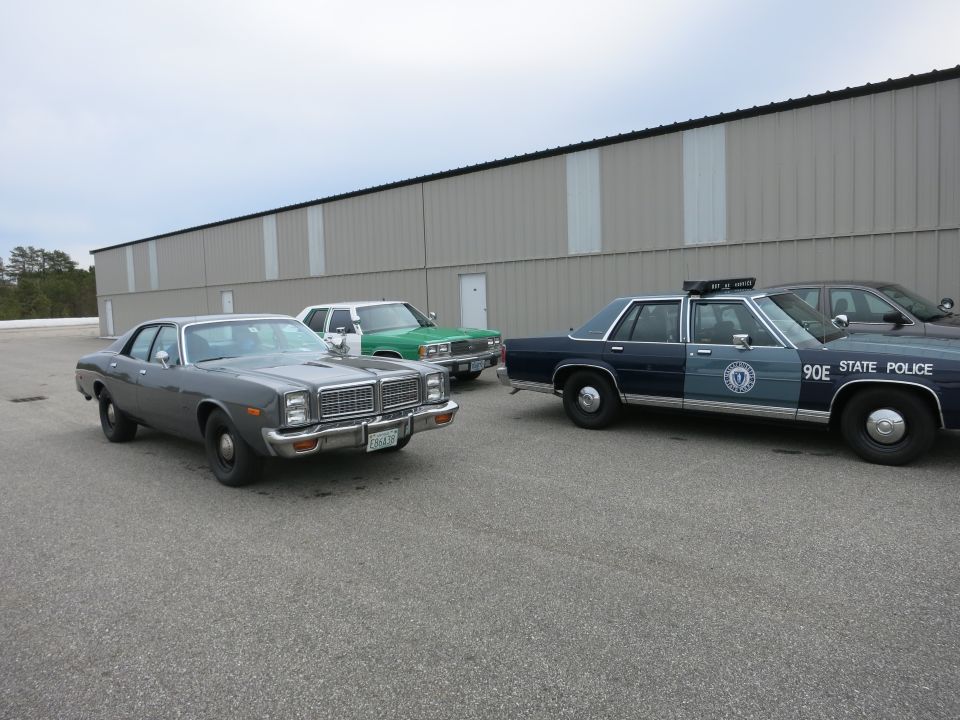 Gray 1977 sedan parked next to a green sedan and a police car