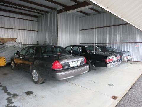 1991 Ford LTD Crown Victoria - Three sedans are parked side-by-side inside a metal-clad garage structure.