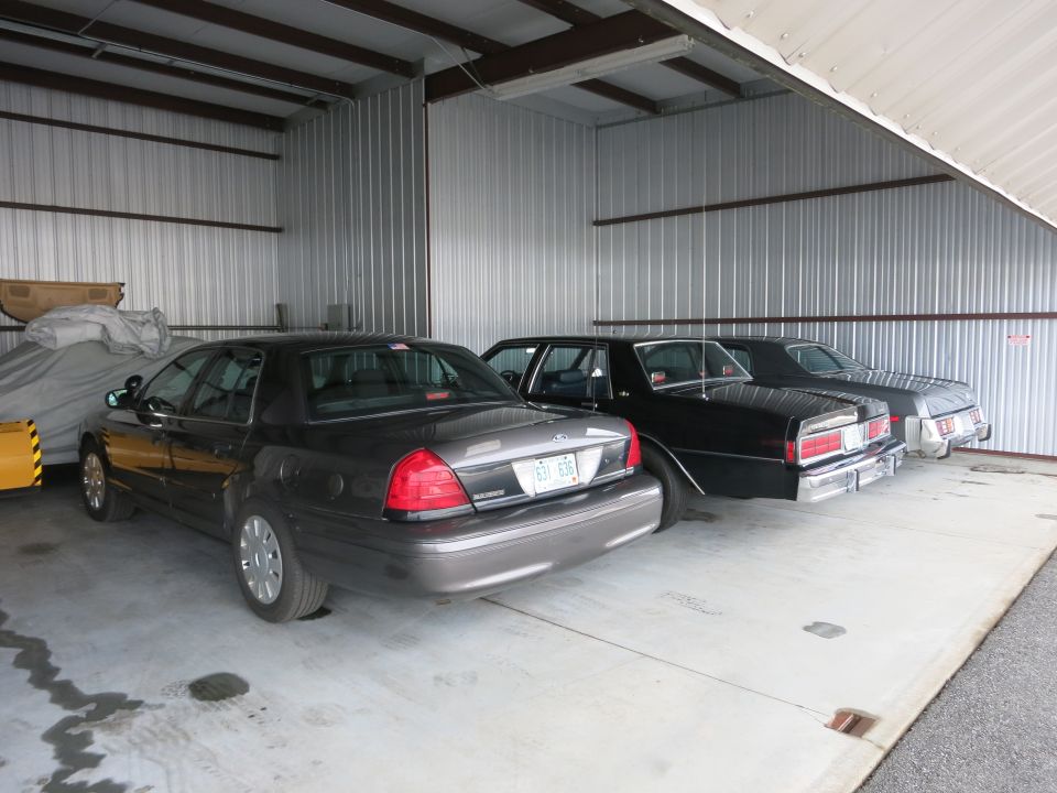 Dark gray sedan in foreground, black sedan behind it, light gray sedan behind that, all parked in a metal garage
