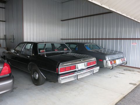 1991 Ford LTD Crown Victoria - Two sedans are parked side-by-side inside a corrugated metal garage.