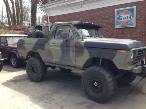 1979 Ford Bronco - This lifted 1979 Ford Bronco sports a camouflage paint scheme and oversized off-road tires, parked beside another vehicle.