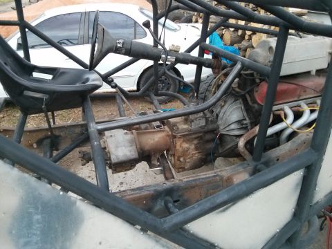 1986 Ford Bronco - The chassis of a custom-built vehicle is shown, with a white car visible in the background.