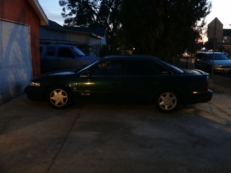 Dark green sedan parked next to a garage, with a blue pickup truck behind it