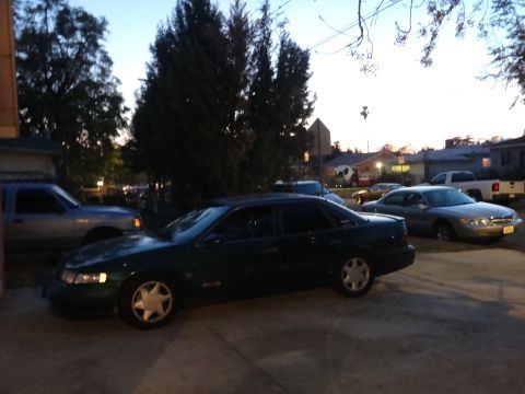 1993 Ford Taurus - A dark green 1993 Ford Taurus is parked in a driveway with other vehicles visible.