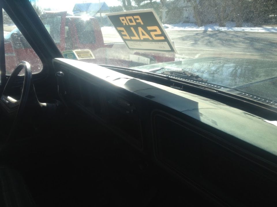 Interior view of a vehicle with a "FOR SALE" sign on the windshield; another vehicle is visible outside