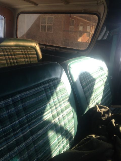 1979 Ford Bronco - Interior view of plaid seats in a vehicle, with a reflection of a brick building visible in the rear window.
