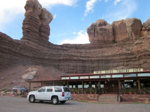 1991 Ford LTD Crown Victoria - A white SUV is parked in front of the Twin Rocks Trading Post, with distinctive layered rock formations towering behind it.