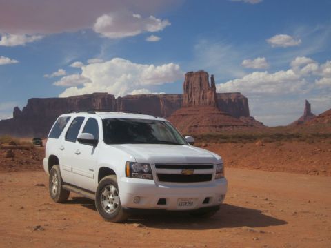 1991 Ford LTD Crown Victoria - A white Chevrolet Tahoe is parked on a dirt road in Monument Valley, Utah, with iconic rock formations under a cloudy sky.