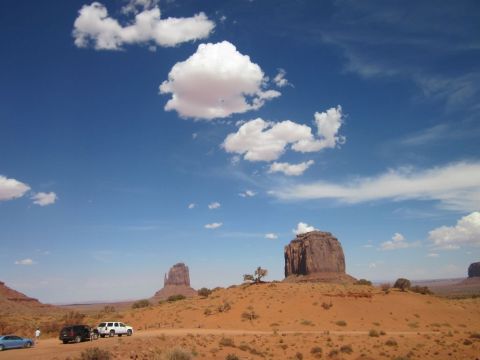 1991 Ford LTD Crown Victoria - Several vehicles are parked on a dirt road in Monument Valley under a bright blue sky with scattered clouds.