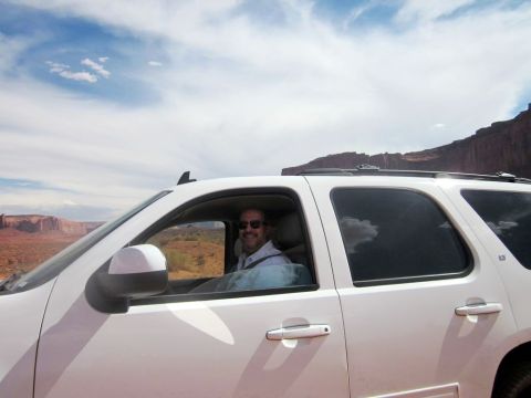 1991 Ford LTD Crown Victoria - Man drives a white SUV through Monument Valley under a cloudy sky.
