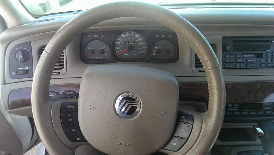 Tan dashboard and steering wheel of a 2000 Mercury Grand Marquis, showing the instrument cluster and radio