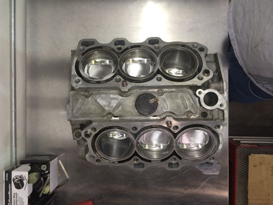 Engine block with six cylinders and pistons, on a metal workbench