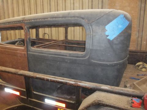 1929 Ford Sedan - The side of a vintage car body, appearing to be a sedan, is loaded onto a trailer inside a building.