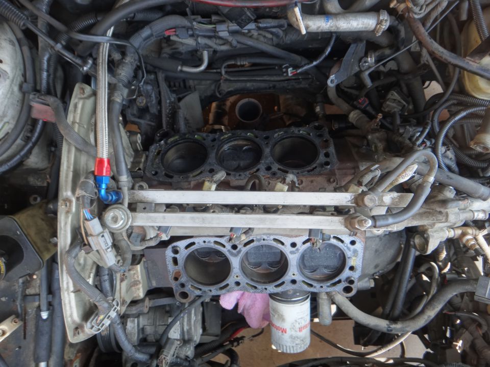 Engine block with cylinder heads removed, showing pistons and gasket remnants. Oil filter visible