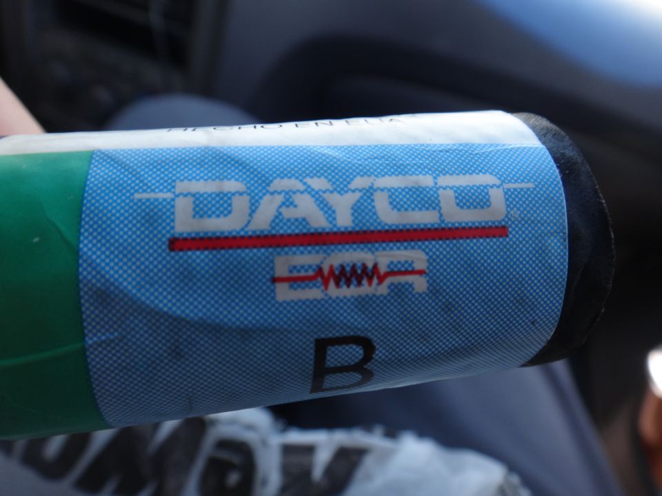 Dayco logo on a green and blue labeled cylindrical part. Part has a red line and a wavy graphic